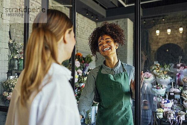 Glückliche schwarze Unternehmerin steht in einem Blumenladen und verkauft frische Blumen an Kunden. Junge blonde Mädchen kaufen einen frischen Blumenstrauß von Florist. Lächelnde afrikanische Frau Botaniker  Verkauf von Blumen