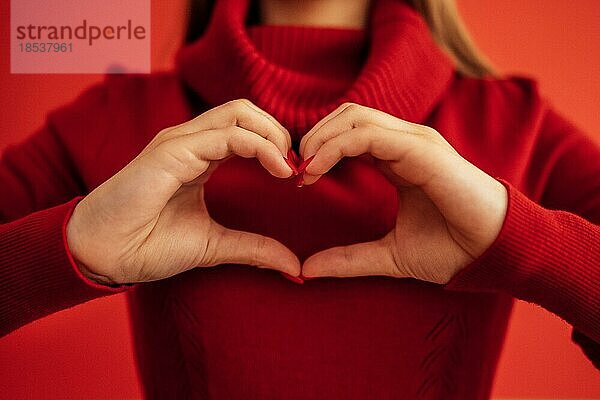 Weibliche Hände bilden eine Herzform. Hände eines jungen weißen Mädchens mit einer schönen leuchtend roten Maniküre. Nahaufnahme. Valentinstag Konzept. Roter Hintergrund