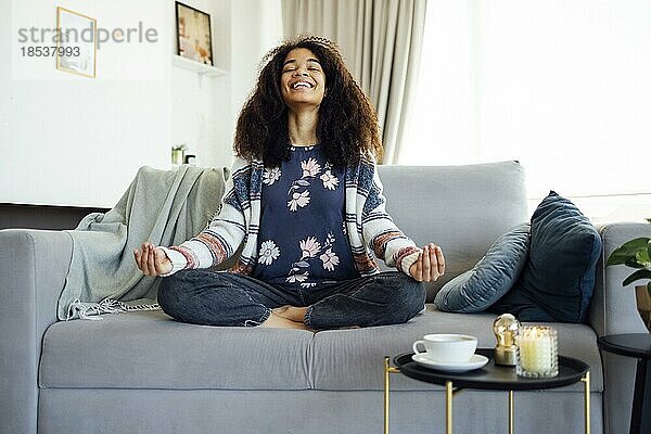 Körper und Geist Gesundheit. Nette lächelnde afroamerikanische Frau lernt Yoga zu Hause auf dem Sofa sitzen