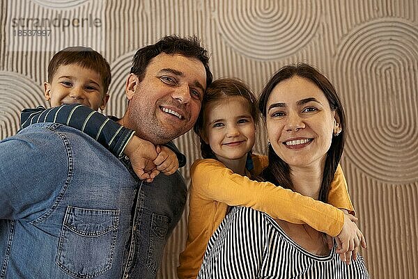 Glückliche Eltern mit Sohn und Tochter posieren in Innenräumen. Schöne Familie Blick in die Kamera in der modernen Wohnung zu Hause  glückliche Elternschaft Familienkonzept