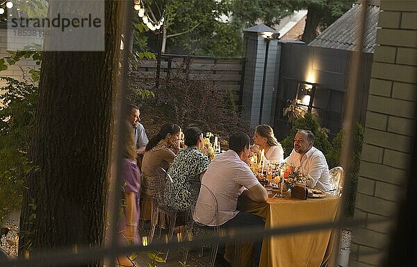 Viele Menschen stoßen an und zeigen einander ihre Sektgläser  während sie eine Hochzeitsfeier im Freien in einem Hinterhofrestaurant bei Sonnenuntergang genießen