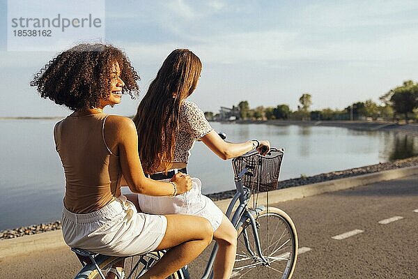 Teenager verschiedener Nationalitäten und unterschiedlichen Aussehens fahren auf Fahrrädern eine Stadtstraße entlang. Junge und positive Mädchen lächeln zusammen. Gesunder Lebensstil und Freundschaft Konzept