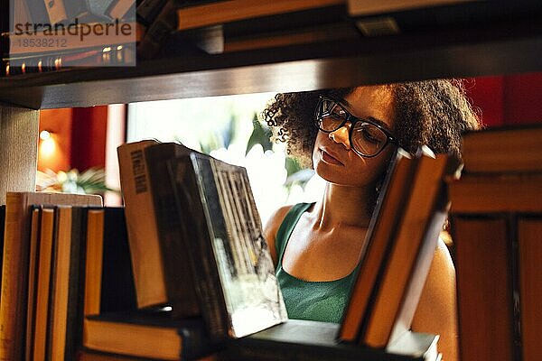 Glückliche afroamerikanische Studentin  die in der Universitätsbibliothek studiert und nach einem Buch sucht  mit Brille