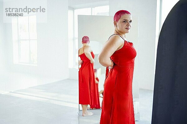 Schöne entspannte Frau in rotem langen Kleid und roten Haaren schaut in den Spiegel. Konzept der Körper positiv