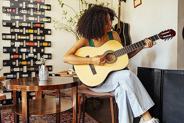 Lächelnde afroamerikanische junge Frau spielt akustische Gitarre. Mädchen spielt die Gitarre