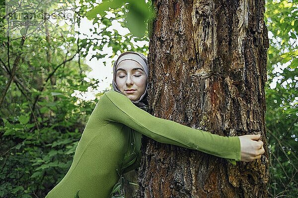 Muslimisches Teenagermädchen umarmt einen Baum. Close up Porträt einer jungen Frau in einem Hijab und Freizeitkleidung im Park. Schutz der Umwelt und Pflege von Pflanzen Konzept
