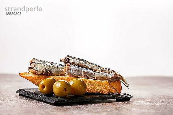 Tapa von Sardinen mit Tomaten und Oliven auf schwarzem Schiefer und weißem Hintergrund typisch spanisch