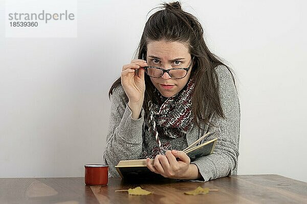 Junge brünette Frau mit langen Haaren und Brille  die ein Buch liest  ihre Brille hält und in die Kamera schaut  vor einem weißen Hintergrund