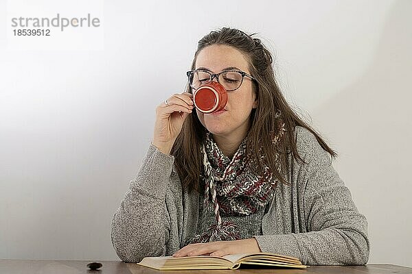 Junge brünette Frau mit langen Haaren und Brille trinkt Kaffee beim Lesen eines Buches.weißer Hintergrund und copy space
