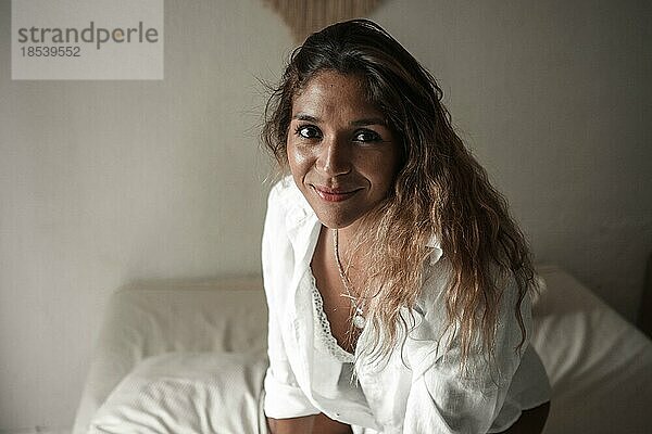 Glückliche junge Latina lächelt in die Kamera und liegt auf ihrem Bett. Gesunder Lebensstil Konzept
