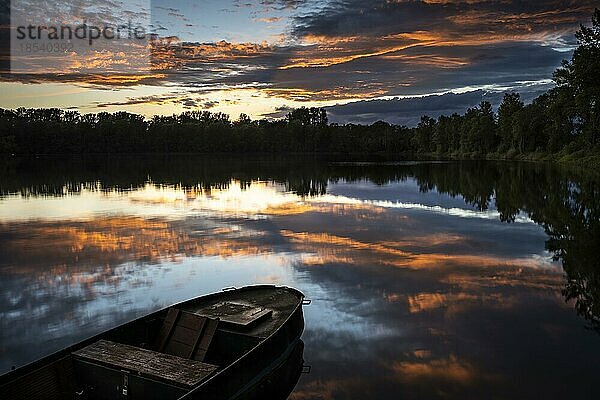 Ein kleines Boot in einem See bei Sonnenuntergang mit farbigen Wolken in orange am Himmel. Der Himmel spiegelt sich im ruhigen See. Rhein-Neckar-Kreis  Baden-Württemberg  Deutschland  Europa