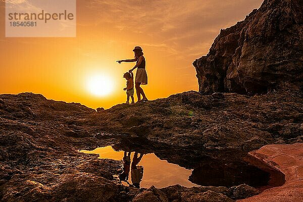 Silhouette von Mutter und Sohn zu Fuß in den Sonnenuntergang am Strand von Tacoron in El Hierro  Kanarische Inseln  Urlaub Konzept  orange Sonnenuntergang  zu Fuß durch das Meer zeigt den Weg