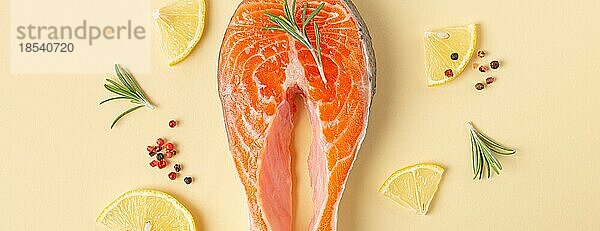 Ungekochte rohen frischen Fisch Lachssteak Draufsicht auf beige Pastell Hintergrund mit Rosmarin  Zitrone Keile und Gewürze  Delikatesse gesunden Fisch Kochen und Ernährung Konzept flach legen