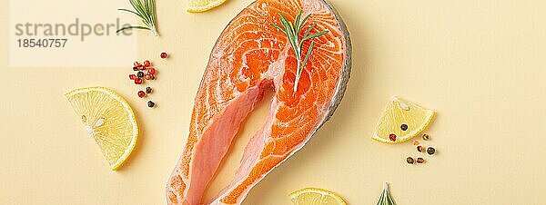 Ungekochte rohen frischen Fisch Lachssteak Draufsicht auf beige Pastell Hintergrund mit Rosmarin  Zitrone Keile und Gewürze  Delikatesse gesunden Fisch Kochen und Ernährung Konzept flach legen