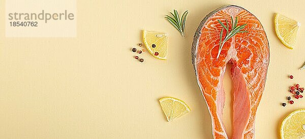 Ungekochte rohen frischen Fisch Lachssteak Draufsicht auf beige Pastell Hintergrund mit Rosmarin  Zitrone Keile und Gewürze  Delikatesse gesunden Fisch Kochen und Ernährung Konzept flach legen Raum für Text