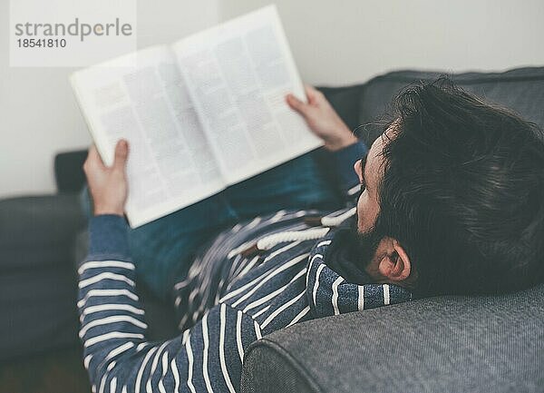 Mann entspannt sich auf der Couch und liest eine Zeitschrift oder Zeitung