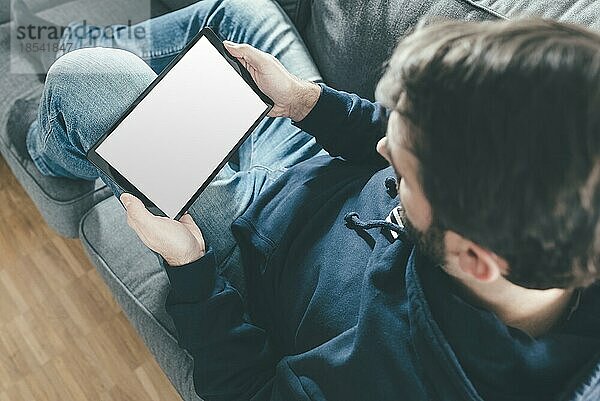 Blick von oben auf einen Mann  der sich auf einer Couch entspannt und einen Tablet-Computer benutzt