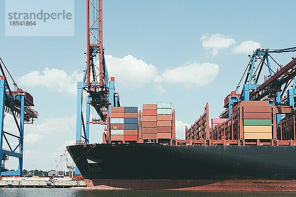 Vorderteil eines großen Containerschiffs am Pier unter Portalkränen gegen blaün Himmel