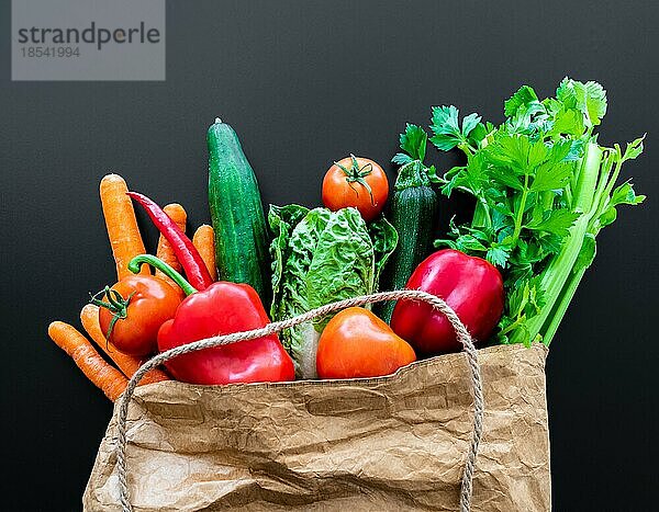 Draufsicht auf frisches Bio-Gemüse  das auf dem Wochenmarkt in einer braunen Papiertüte gekauft wurde  vor dunklem Tisch-Hintergrund