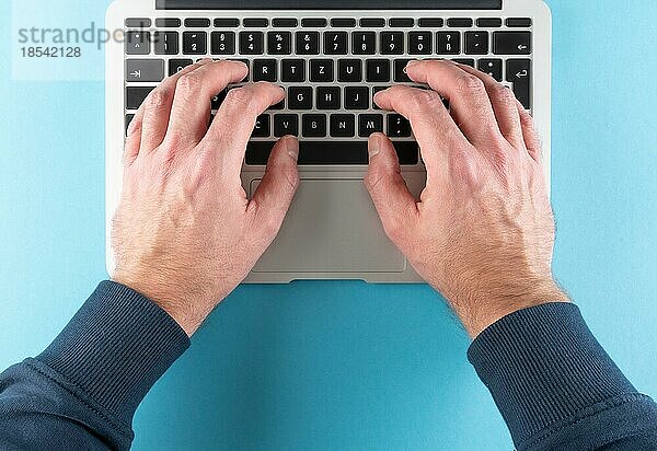 Draufsicht auf die Hände eines Mannes  der auf einem Laptop-Computer auf blauem Schreibtisch-Hintergrund tippt