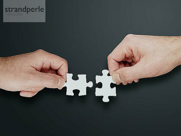 Hände von zwei Personen  die zwei Puzzleteile zusammensetzen  Lösungen finden und Teamwork-Konzept