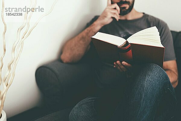 Nahaufnahme eines kaukasischen Mannes  der sich zu Hause auf dem Sofa ausruht und ein Buch liest