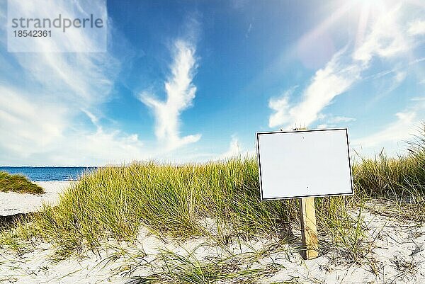 Wegweiser mit Schriftfeld am breiten Sandstrand vor Meer und blauem Himmel