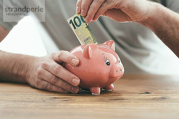 Nahaufnahme eines Mannes  der Geld in ein Sparschwein auf einem Holztisch legt  Geld sparen oder Finanzkonzept