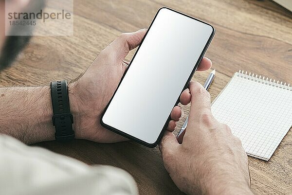 Blick über die Schulter auf einen Mann  der an einem Holztisch sitzt und ein Smartphone benutzt