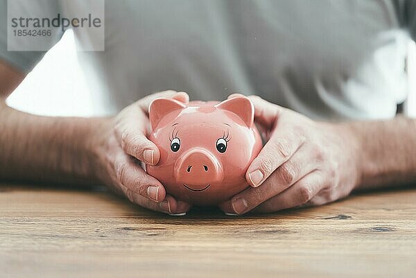 Nahaufnahme eines Mannes  der ein Sparschwein mit beiden Händen an einem Holztisch hält  Konzept des Geldsparens und der Finanzen