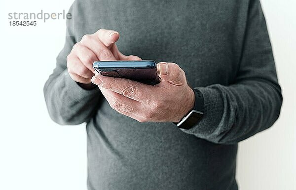 Mittelteil eines Mannes mit Smartphone in der Hand vor einer weißen Wand