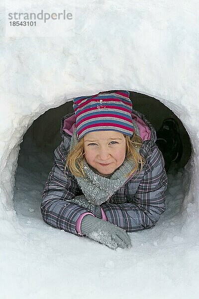 Mädchen schaut aus einer Schneehöhle im Hochformat