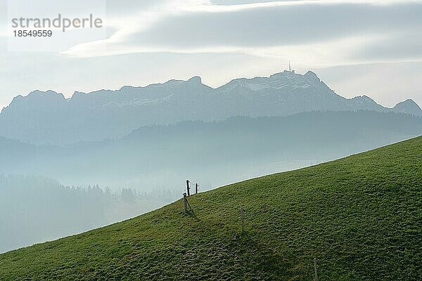 Idyllische und friedliche Berglandschaft mit einem Holzzaun an einem grasbewachsenen Hang und einer tollen Aussicht auf das Alpsteingebirge und das Appenzellerland in den Schweizer Alpen im Hintergrund