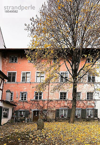 Innenhof mit alter rustikaler Hausfassade in typischer Nordostschweizer Architektur und herbstlich gefärbten Bäumen und Blättern im Vordergrund im idyllischen Dorf Neunkirch bei Schaffhausen in der Schweiz