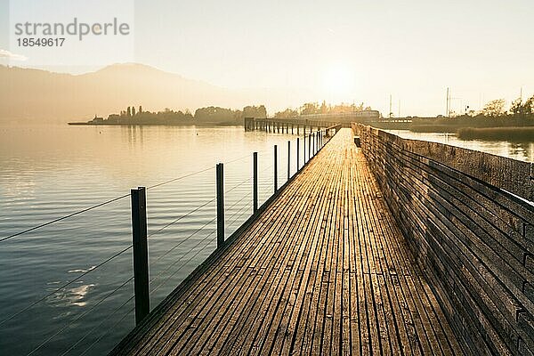 Ein horizontaler Blick auf eine lange hölzerne Promenade Pier über Wasser in goldenen Abendlicht mit einer Berglandschaft Silhouette im Hintergrund