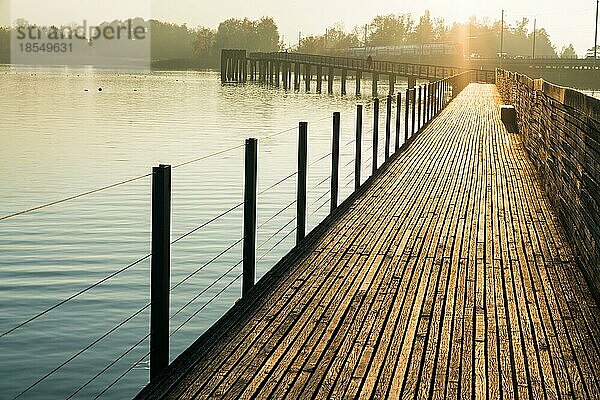 Langer Holzsteg und Promenade über dem Zürichsee bei Rapperswil im goldenen Abendlicht mit Silhouette der Berge im Hintergrund