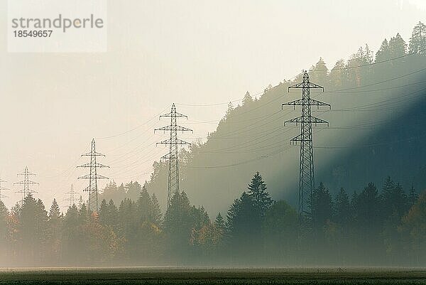 Stromleitungen und Gitterkreuze an einem dunstigen Morgen in einem Bergtal mit Herbstfarbe Wald rund um in einem Bergtal in der Schweiz