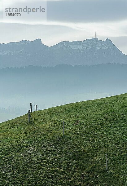 Idyllische und friedliche Berglandschaft mit einem Holzzaun an einem grasbewachsenen Hang und einer tollen Aussicht auf das Alpsteingebirge und das Appenzellerland in den Schweizer Alpen im Hintergrund
