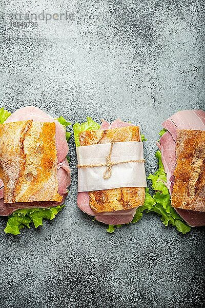 Frische Ciabatta-Sandwiches mit Schinken  Käse  Salat auf Stein Beton Hintergrund  Nahaufnahme  Draufsicht. Herstellung gesunder Sandwiches für Snack oder Mittagessen Konzept