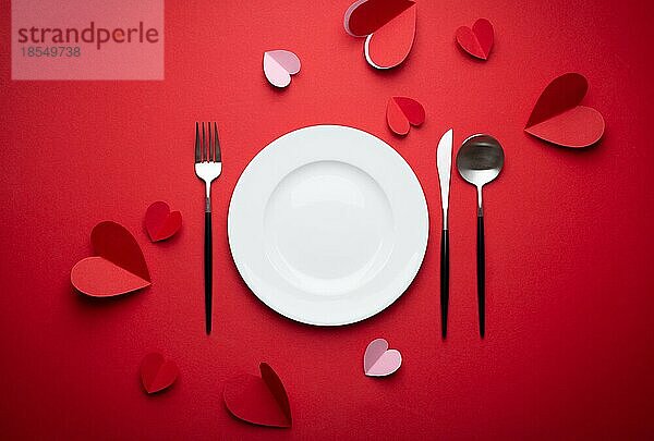 Romantisches Abendessen im Restaurant am Valentinstag  Papierkunst. Weiß leeren Teller  Löffel  Gabel  Messer auf rotem Hintergrund mit Papier Herzen. Valentinstag Datum Konzept Handwerk Origami  Platz für Text