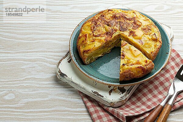 Hausgemachte spanische Tortilla mit einer Scheibe geschnitten Omelett mit Kartoffeln auf dem Teller auf weißem Holz rustikalen Hintergrund Draufsicht. Traditionelles Gericht von Spanien Tortilla de patatas für Mittagessen oder Snack  oben