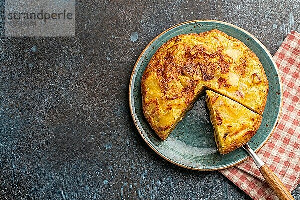 Hausgemachte spanische Tortilla mit einer Scheibe geschnitten Omelett mit Kartoffeln auf einem Teller auf Stein rustikalen Hintergrund Draufsicht. Traditionelles Gericht von Spanien Tortilla de patatas für Mittagessen oder Snack  Platz für Text