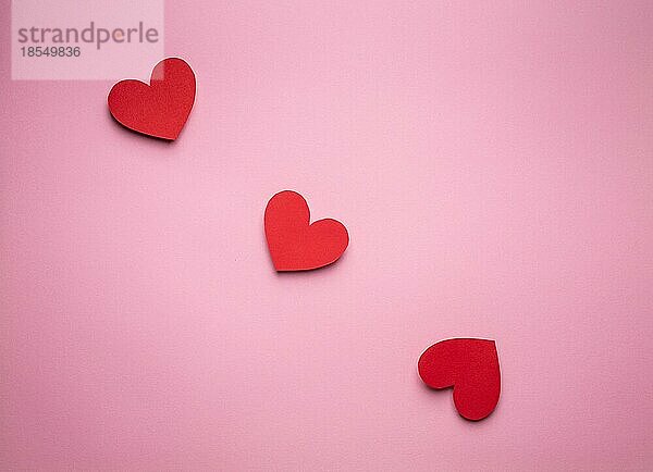 Drei rote Herzen in einer Reihe aus Papier geschnitten auf rosa Hintergrund  Handwerk OrigamiStil von oben. Romantische Valentinstag Liebe Konzept. Verschiedene Größe Herzen Draufsicht  Papier Kunst Design