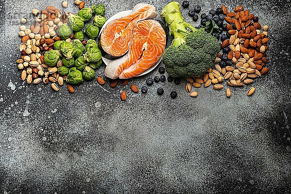 Verschiedene Lebensmittel für die Gesundheit des Gehirns und ein gutes Gedächtnis: frischer Lachs  Gemüse  Nüsse  Beeren auf einem steinernen Hintergrund. Gesunde frische Produkte zur Förderung der Gehirnleistung  Draufsicht mit Platz für Text