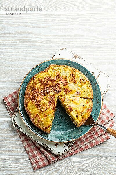 Hausgemachte spanische Tortilla mit einer Scheibe geschnitten Omelett mit Kartoffeln auf dem Teller auf weißem Holz rustikalen Hintergrund Draufsicht. Traditionelles Gericht von Spanien Tortilla de patatas für Mittagessen oder Snack  oben