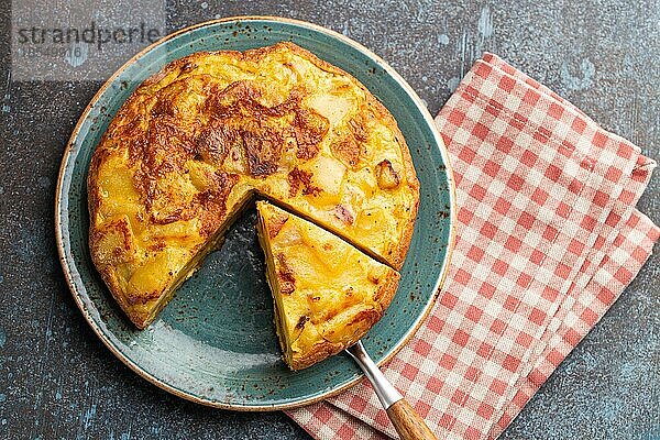 Hausgemachte spanische Tortilla mit einer Scheibe geschnitten Omelett mit Kartoffeln auf einem Teller auf Stein rustikalen Hintergrund Draufsicht. Traditionelles Gericht von Spanien Tortilla de patatas für Mittagessen oder Snack  Overhead