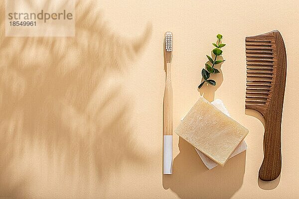 HolzHaarkamm Öko Bambus Zahnbürste  natürliche Seife auf beige Pastell Hintergrund mit tropischen Blättern Schatten am sonnigen Morgen. Waschen und Zahnreinigung Morgen Routine  Null Abfall Leben  Draufsicht