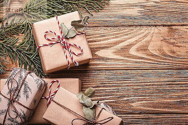 Eingepackte Weihnachtsgeschenke flach legen Zusammensetzung mit Tannenzweig auf hölzernen Hintergrund. Weihnachten und Neujahr Geschenkboxen Draufsicht mit Freiraum für Textvorlage