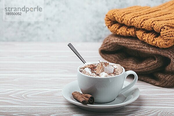 Cozy Winter Zusammensetzung  Tasse mit heißer Schokolade oder Kakao mit Marshmallow und Stapel von warmen gestrickte Kleidung auf weißem Holz rustikalen Hintergrund. Gemütliche und weiche Winter zu Hause  freier Raum für Text