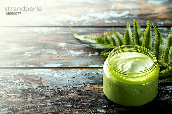 Kosmetische Creme in einem Behälter auf einem hölzernen Hintergrund mit grünem Blatt  Naturkosmetik  Bio Hautpflegeprodukt Konzept. Hausgemachte Creme für Gesicht und Körperpflege  Hintergrund mit Kopie Raum Draufsicht